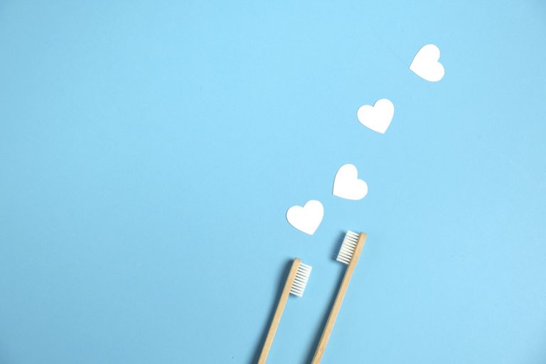 Illustration of two wooden bamboo toothbrushes below two white hearts on a blue background
