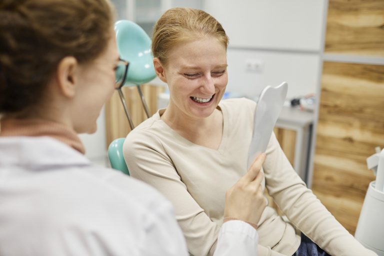 Female patient sitting at the dentist, looking in a mirror, happy with her teeth