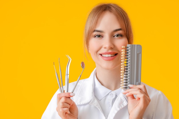 female dentist holds dental tools and a chart with varying colors of teeth
