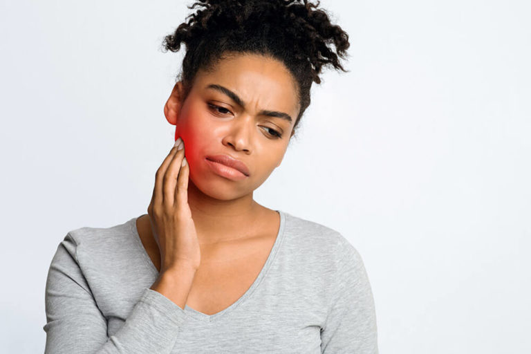 woman holding her cheek, as if she has tooth pain