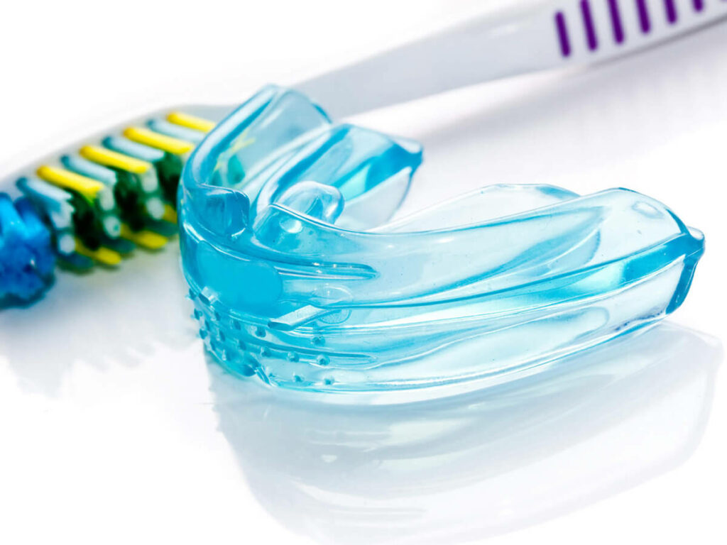 Close-up of a blue dental mouthguard with a toothbrush in the background.