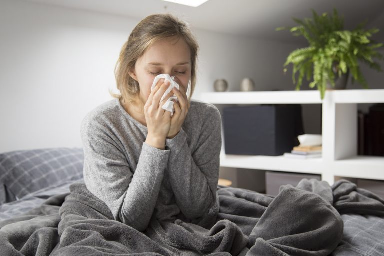 Sick woman sitting in bed, blowing nose with tissue
