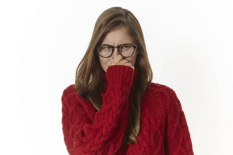 Female in red sweater with glasses, pinching her nose shut as if she just smelled something bad