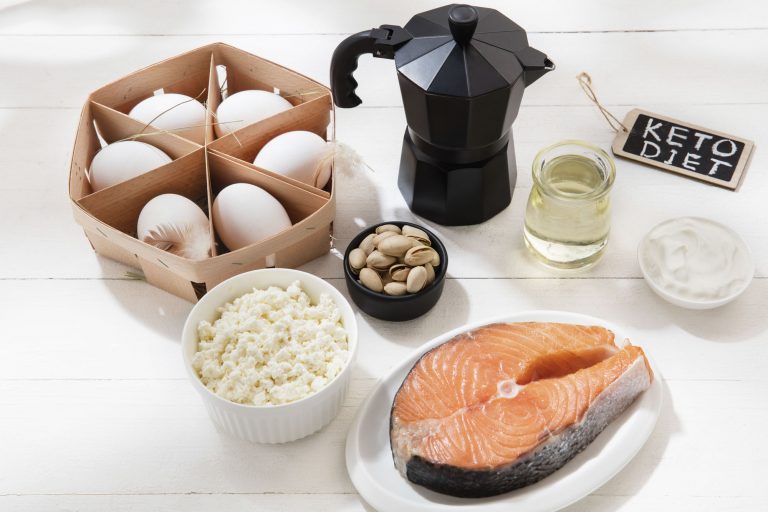 Food items typically part of the keto diet, including eggs, fish, nuts, oil, pistachios and a coffee pot on a table
