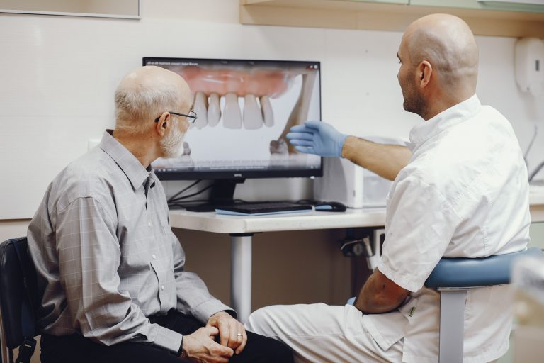 Elderly man sitting in the dentist's office looking at a photo of a mouth with a missing tooth