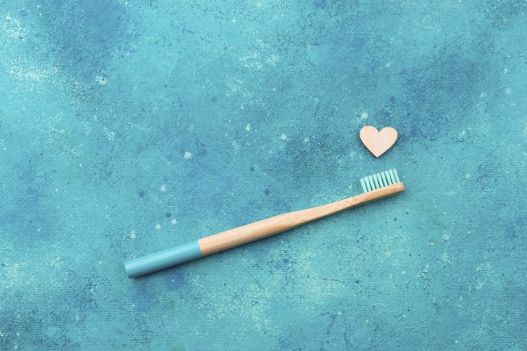 Illustration of a tan and blue toothbrush on a turquoise background with a small wooden heart above the toothbrush