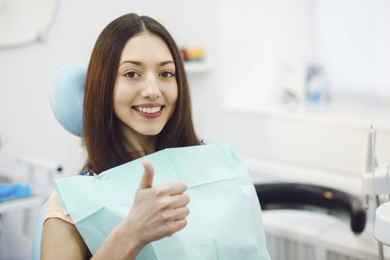 Woman sitting, showing thumbs up at the dentist