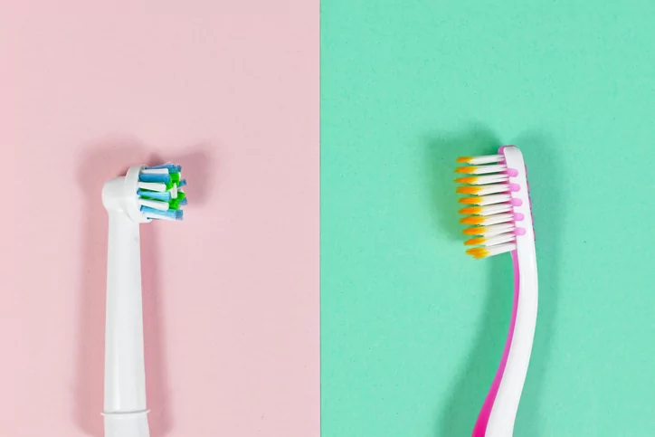 Side-by-side comparison of an electric toothbrush head on a pink background and a manual toothbrush on a green background.